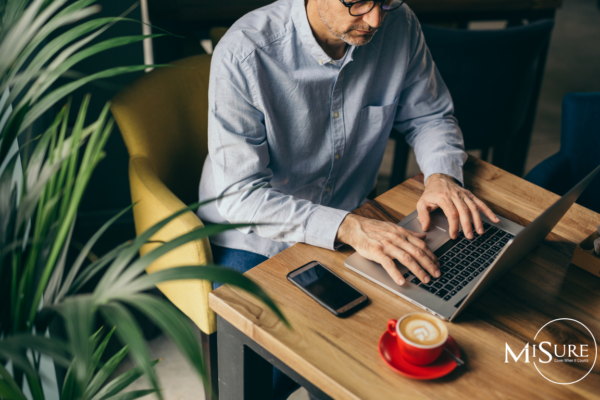Man working with laptop at desk with red coffee cup